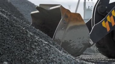 Bulldozer scoop takes gravel from heap at mining quarry closeup. Excavator operates with small rocks at construction site