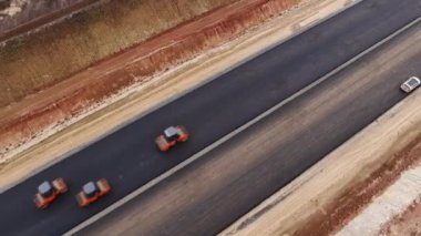 Timelapse of powerful double drum rollers driving along new road lane pressing asphalt at countryside aerial view