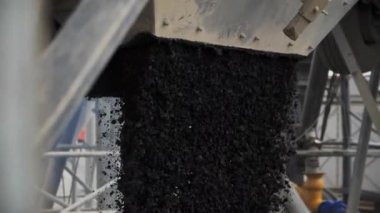 Filling truck body with hot mix asphalt poured down from funnel at station closeup. Modern material used at roadworks