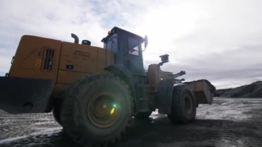 İnşaat alanında aydınlık bulutlu gökyüzüne karşı güçlü buldozer sürücüleri. Araç alacakaranlıktaki fabrikaya gidiyor.