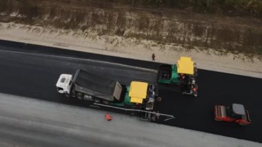 ALMATY, KAZAKHSTAN - 17 Şubat 2023: Asfalt asfalt kaldırım makineleri kırsal otoyol şeridini inşaatçıların kontrolündeki hava görüşüyle kaplıyor. 17 Şubat 'ta Almaty' de yol çalışması için inşaat teknolojisi