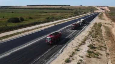 ALMATY, KAZAKHSTAN - 17 Şubat 2023: Yaz günü hava manzarasında yeni otoyol şeridine çöp kamyonları ve asfalt kaldırım. 17 Şubat 'ta Almaty' de yol çalışması makineleri kırsal kesimde faaliyet gösteriyor.