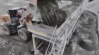 Kazıcı, taş ocağı hava görüşündeki kovadan ayrıştırma makinesine toprak döküyor. İnşaat malzemeleri kazma teknolojisi