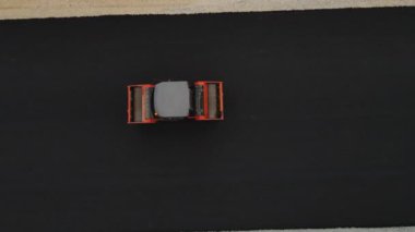 Paten kamyonu, inşaat alanının üst manzarasında, yol şeridi yüzeyinde taze asfalt eziyor. Yol çalışmaları ve kaldırımlar sırasında kullanılan makineler