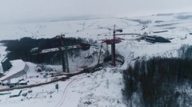 Karlı, içi boş hava manzaralı inşaat alanında nakliye köprüsü bölümü ve kule vinçleri. Makineli kış manzarası