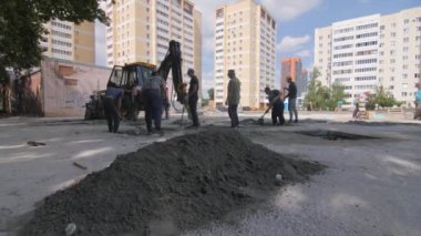 ALMATY, KAZAKHSTAN - Haziran 06 2022: İşçiler inşaat alanına beton dökmek için kürekle toprak artıklarını temizliyorlar. Kazıcı parka beton uygulamak için çukur kazıyor