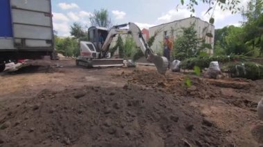 ALMATY, KAZAKHSTAN - Haziran 06 2022: Backhoe şehir parkında işçilerin kontrolü altında çam ağaçları için çukur kazıyor. Kazıcı şehir bahçesinde çukur kazıyor.