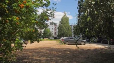 ALMATY, KAZAKHSTAN - Haziran 06 2022: Apartman binaları ve yeşil ağaçların yakınındaki otopark. Arabalar yemyeşil şehir parkında. Doğa ve kentsel yapı