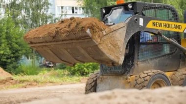 ALMATY, KAZAKHSTAN - Haziran 06 2022: Kazıcı inşaat alanı hazırlamak için kum kalıntılarını yığının üzerine döküyor. Buldozer, yaz günü parkta kovayla kum doldurur.
