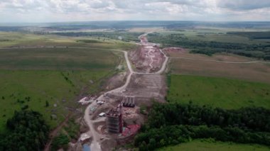 İnşaat alanındaki boş hava manzaralı bina iskeleleri ve vinçlerle nakliye köprüsü desteği. Peyzajlı bölgede otoyol inşaatı