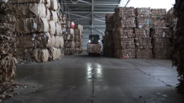 ALMATY, KAZAKHSTAN - 17 Nisan 2023: Depo koridoru boyunca atık kağıt paketiyle yanan farlı forklift yükleyici. Geri dönüşüm fabrikası çöplüğünde makine nakliye çöplüğü