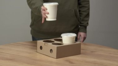 Kadın, ahşap masadaki plastik bardağı karton tutacağa koyuyor. Paketlenmiş restoranlar için tek kullanımlık konteynırlar.