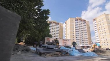 İşçiler ve araçlar yeni konut kompleksine beton kaplama döşemeye çalışıyorlar. Yüksek binalara karşı ağır makineler çalışıyor