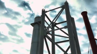 Borulardan parlak güneş ışığıyla aydınlatılmış bulutlu gökyüzüne doğru beyaz bir duman çıkıyor. Kış günü küçük bir kasabada metal şebeke ile çalışan kazan dairesi.
