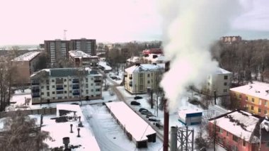 Etrafı yerleşim yerleriyle çevrili kazan dairesinden yoğun beyaz duman çıkıyor. Kış günü hava manzaralı küçük bir kasabada metal şebeke yapısı