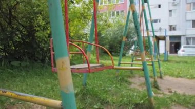 Bahçedeki yeşil çimlere kurulmuş çocuklar için metal salıncaklar. Güneşli yaz gününde, yüksek binaların yakınındaki eski oyun alanı ekipmanları.