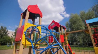 Çocuklar için oyun alanı ekipmanları mavi gökyüzünün altında beyaz bulutlarla eğleniyor. Güneşli yaz gününde yemyeşil ağaçların olduğu bir yerleşim yeri.