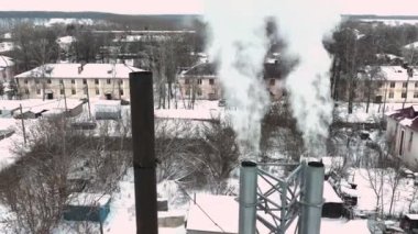Kasvetli kış gününde dumanlı metal borular ve yoğun kazan dairesi dumanı. Endüstriyel bölge hava manzaralı konut binaları