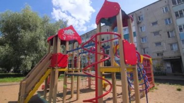 Çocuk parkına kurulmuş çocuklar için eğlence ekipmanları. Güneşli yaz gününde mavi gökyüzünün altında konut binası ve yemyeşil ağaçlar