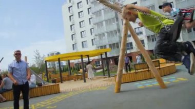 ALMATY, KAZAKHSTAN - 10 Mayıs 2023: Erkekler salıncakta sallanan oğullarını sallıyor özel yerleşim alanlarının oyun alanında eğleniyorlar. Modern parktaki çocuklar için eğlence ve eğlence