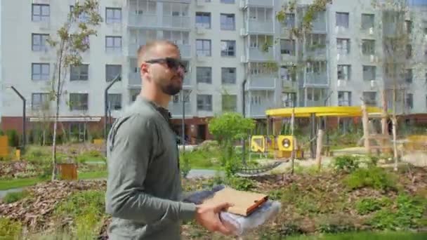 阿尔蒂 哈萨克斯坦 5月10日2023 戴着太阳镜的笑脸男子走过私人住宅建筑群的包裹公园 步行和现代住宿的概念 — 图库视频影像