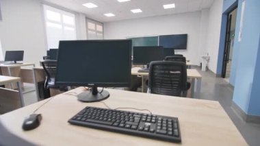 Bilgisayarlar boş IT sınıfındaki küçük ahşap masalarda. Üniversitedeki öğrenciler ve öğretmenler için dijital ekipman