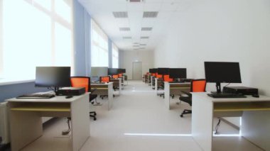 Bilgisayarlı işyerleri boş, uzun ofis öncülüğünde. Çağdaş okulda mobilya ve çalışma yerlerinin olduğu IT sınıfı. Masalardaki bilgisayarlar