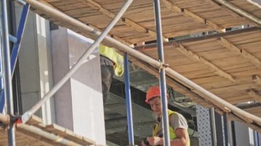 ALMATY, KAZAKHSTAN - 16 Mayıs 2023: Olgun işçi iskeleler üzerinde çalışan bina cephesinin detaylarını vidaladı. Yetenekli bir çalışan, detayları elektrikli tornavidaya bağlar.