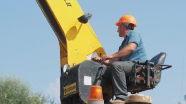 ALMATY, KAZAKHSTAN - 09 Mayıs 2023: Kalifiye çalışan temiz gökyüzüne karşı inşaat alanında vinç kaldırma pozisyonu değiştirdi. Makinenin açık kokpitinde miğferi olan bir inşaatçı