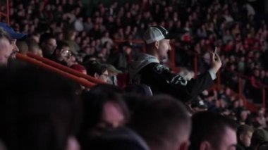 ALMATY, KAZAKHSTAN - 27 Mart 2023: Erkek hayran telefon kullanarak yarışma alanından video çekiyor. Takımlar arasındaki heyecan verici dövüş beklentisiyle kendini adamış bir taraftar kalabalık tribünde duruyor.