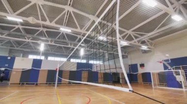 Büyük beyaz voleybol ağı geniş spor salonunu ikiye böler. Gates, arka planda futbol oynadığın için. Lambalar odayı aydınlatıyor.