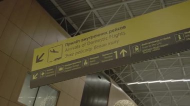 Aydınlatılmış havaalanında asılmış sarı siyah plakalı Yurtiçi uçuşlar. Havaalanının üst katında sallanan ziyaretçilerin parlak işareti.