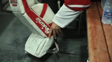 ALMATY, KAZAKHSTAN - 22 Temmuz 2023: Hokey kalecisi tahta bankta bacak koruyucularını ve spor patenlerini çıkarıyor. Oyuncu, bacaklarını yükten rahatlatmak için korumayı kaldırır