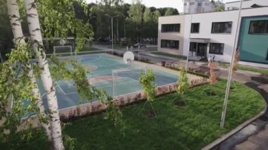 Eğitim kurumunun bölgesindeki yeni renkli spor sahası. Öğrenciler için basketbol sahasını çevreleyen yeşil çimenler ve ağaçlar