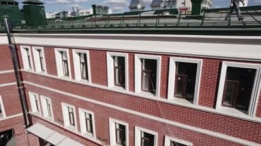 Binada koyu camlı kırmızı tuğla duvarlar var. İnşaat alanında kamusal yapının yükselişi. Güneşli alanda inşaat süreci