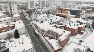 Trafik yolu, çatıları kalın kar tabakasıyla kaplı, inşa edilmiş binadan geçen arabalarla dolu. Kış şehrinin manzarası