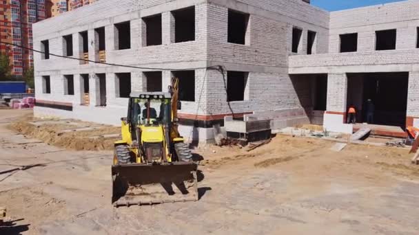 轮式装载机在未完工的公共砖房前的工地上挖土 建筑工人使用推土机的空中视图工作 — 图库视频影像