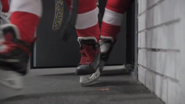 Soyunma odasında buz pateni giyen okul çocukları. Hokey şampiyonası için salonda yürüyen çocuklar arenada düşük açılı şut çekiyorlar.