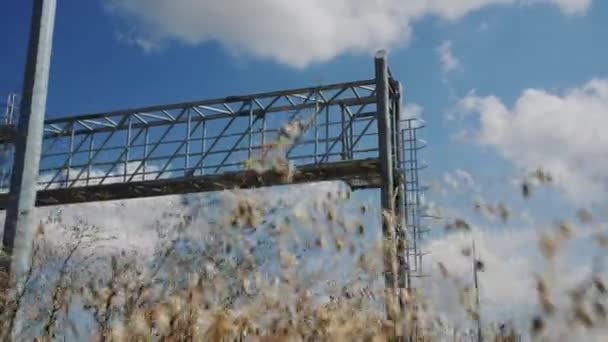 オーバーヘッドのスパンの構造は曇った空に対して国の道の上に歩きます 夏の田舎の労働者のための梯子そして棒が付いている金属のアーチ — ストック動画