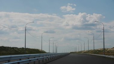 Trafik çitleri ve gökyüzünün altında bulutlu sokak lambaları olan yeni bir yol. Resimli kırsal kesimdeki alçak tepeler arasında çağdaş otoyol