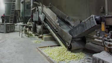 Taşıyıcı makine fabrikada granüle malzeme üretiyor. Büyük çelik makine patenleri döndürerek granülleri büyük kutunun içine döker.