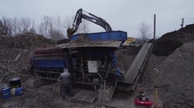 Çalışan, toprak filtreleme makinesinin çalışmasını kontrol ediyor. Çukurun hava görüntüsünde kazıcı var. İşçi ve modern makineler mevduat çıkarma ocağında