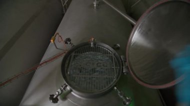 İşçi, fabrika atölyesinde kimyasal maddelerle metal tankın kapağını açıyor. Çalışan, rezervuarın içini köpükle gösterir