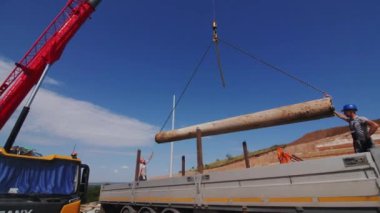 ALMATY, KAZAKHSTAN - 16 Ağustos 2023: İnşaat alanındaki kamyon gövdesinde vinç yükleme borusunu kontrol eden miğferli işçiler. Kanalizasyon sistemi açık havada taşınmak için hazırlanıyor.