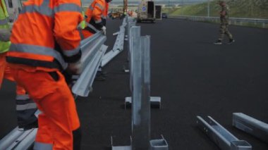 ALMATY, KAZAKHSTAN - 16 AĞUSTOS 2023: İnşaatçılar yavaş çekimde medyan çitleri için kordona metal kalas monte ettiler. İşçiler yol işlerinde desteklere uzun detaylar verdiler