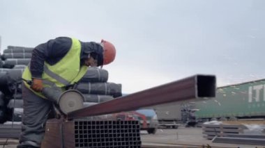 ALMATY, KAZAKHSTAN - 10 Ekim 2023: Miğfer giyen işçiler profil borusunu kesmek için dairesel testere kullanıyor. Adam, profil borularını inşaat amaçları için gerekli boyuta ayarlar