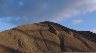 İnşaat alanında gökyüzüne doğru uzanan devasa kum dağları. Güneş ışığıyla yıkanmış devasa kum yığını inşaat sahasında duruyor.