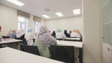 ALMATY, KAZAKHSTAN - 13 Şubat 2023: Türbanlı Müslüman kadınlar konferans salonundaki masalarda otururlar. Kadınlar parlak sınıflarda masalarda oturan öğretim üyelerinin raporlarını dikkatle dinlerler.