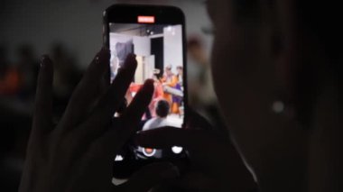 ALMATY, KAZAKHSTAN - 27 Eylül 2023: Genç kadın cep telefonundaki performans videosunu kaydediyor. Karanlık odadaki kadın silueti hatırlamak için şov videosu çekiyor