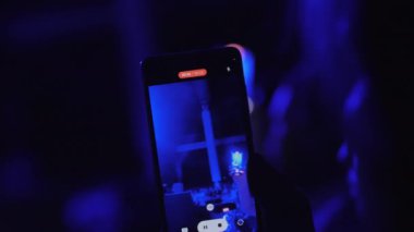 İzleyiciler gece kulübünde akıllı telefondan müzik grubu performansını kaydediyor. Davulcu telefon ekranı aracılığıyla sahne görünümünde enstrümantal set çalar
